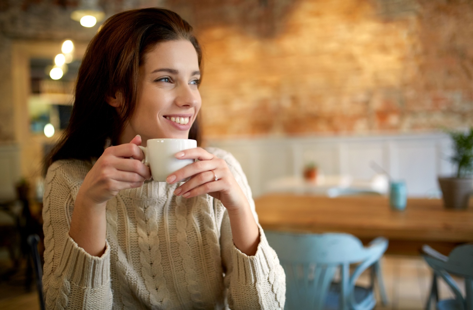 A person holds a coffee cup and smiles with bright teeth.