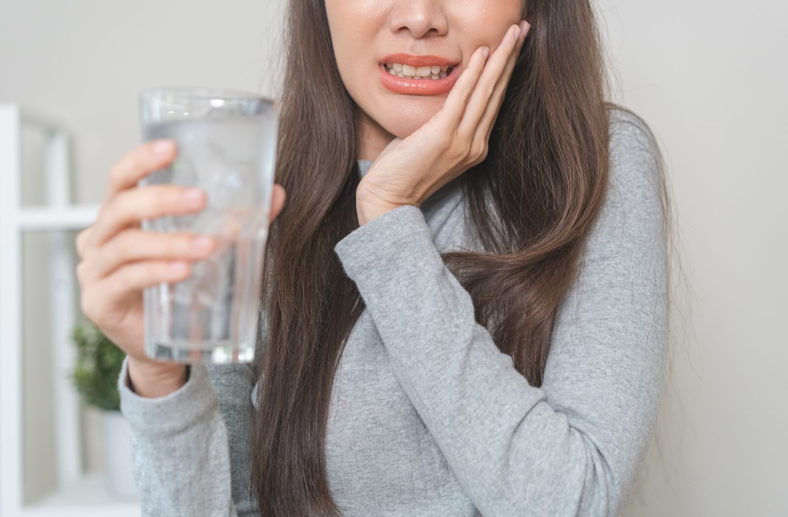 A person holding a glass of ice water while touching their cheek in discomfort due to tooth sensitivity