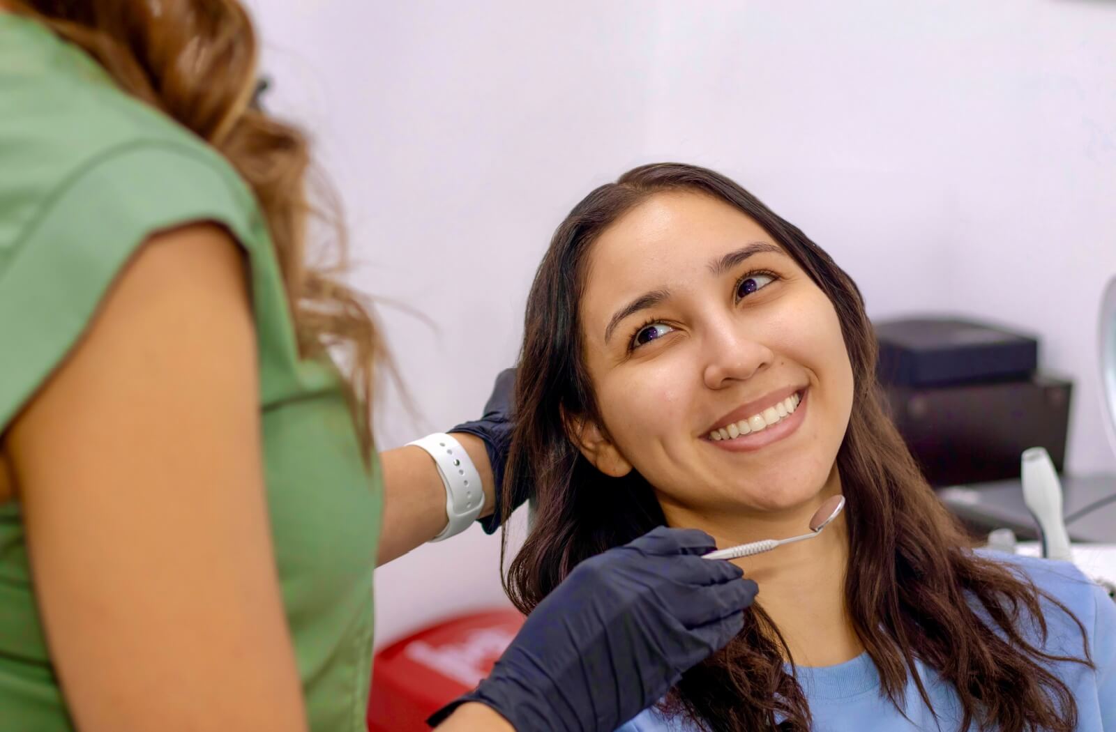 A smiling dental patient in a consultation with a dentist holding a dental mirror