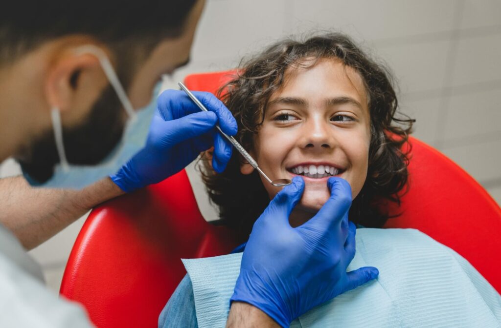 A young child smiling at the dentist during a professional dental cleaning as the dentist holds a mouth mirror.