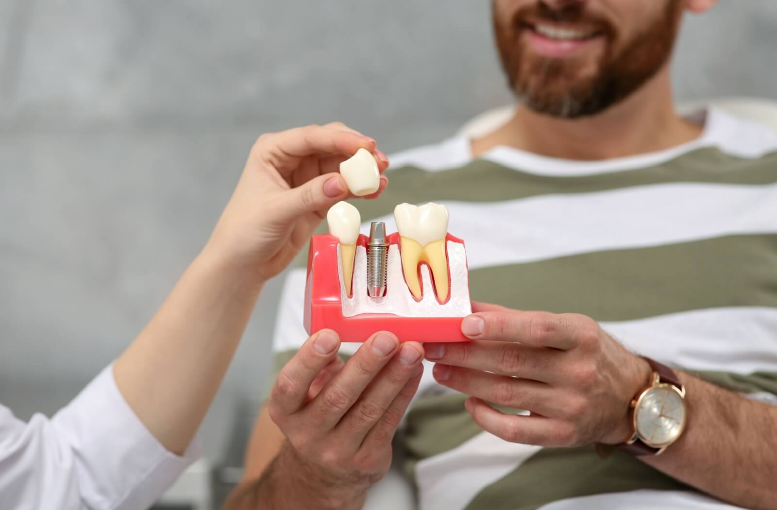 A person is shown on a model where the tooth crown will go, atop a cross section of a dental implant and abutment.