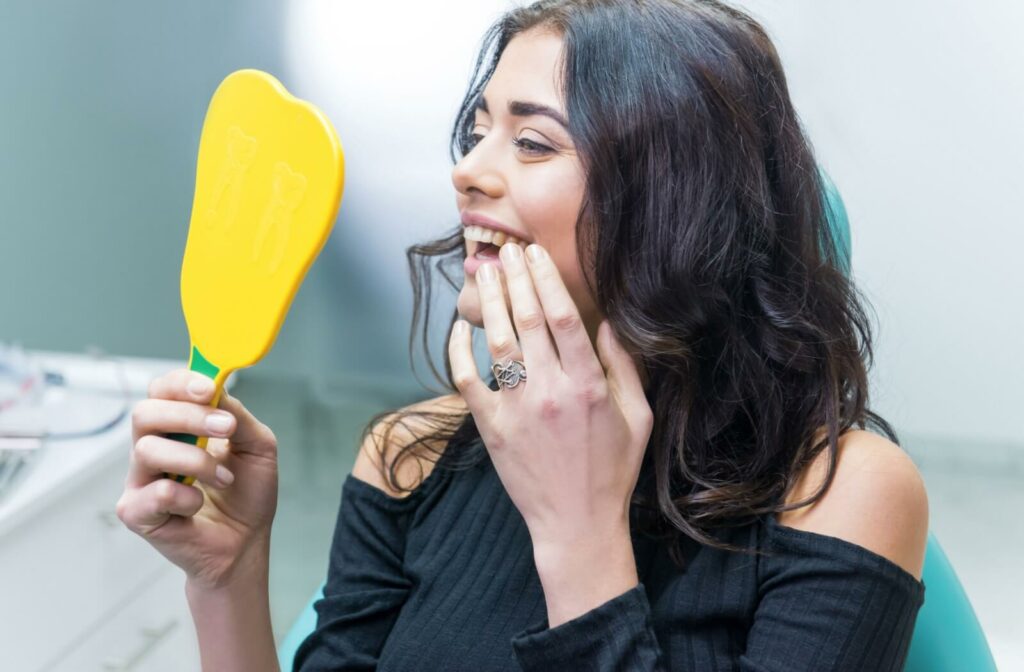 Someone admires their new teeth in the mirror after getting them restored.