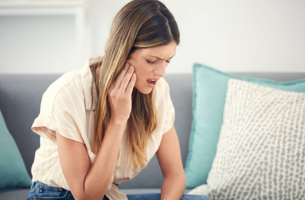 An impacted wisdom tooth causes a person sitting at home to rub their jaw in pain.