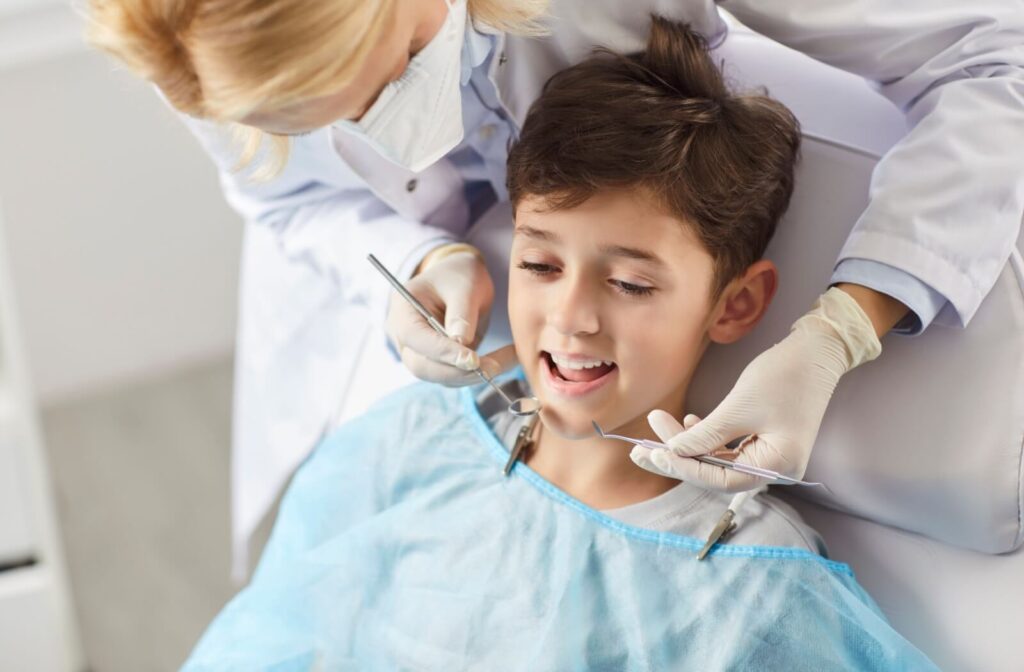 A child sits in a dental chair while a dentist examines his teeth using dental instruments.