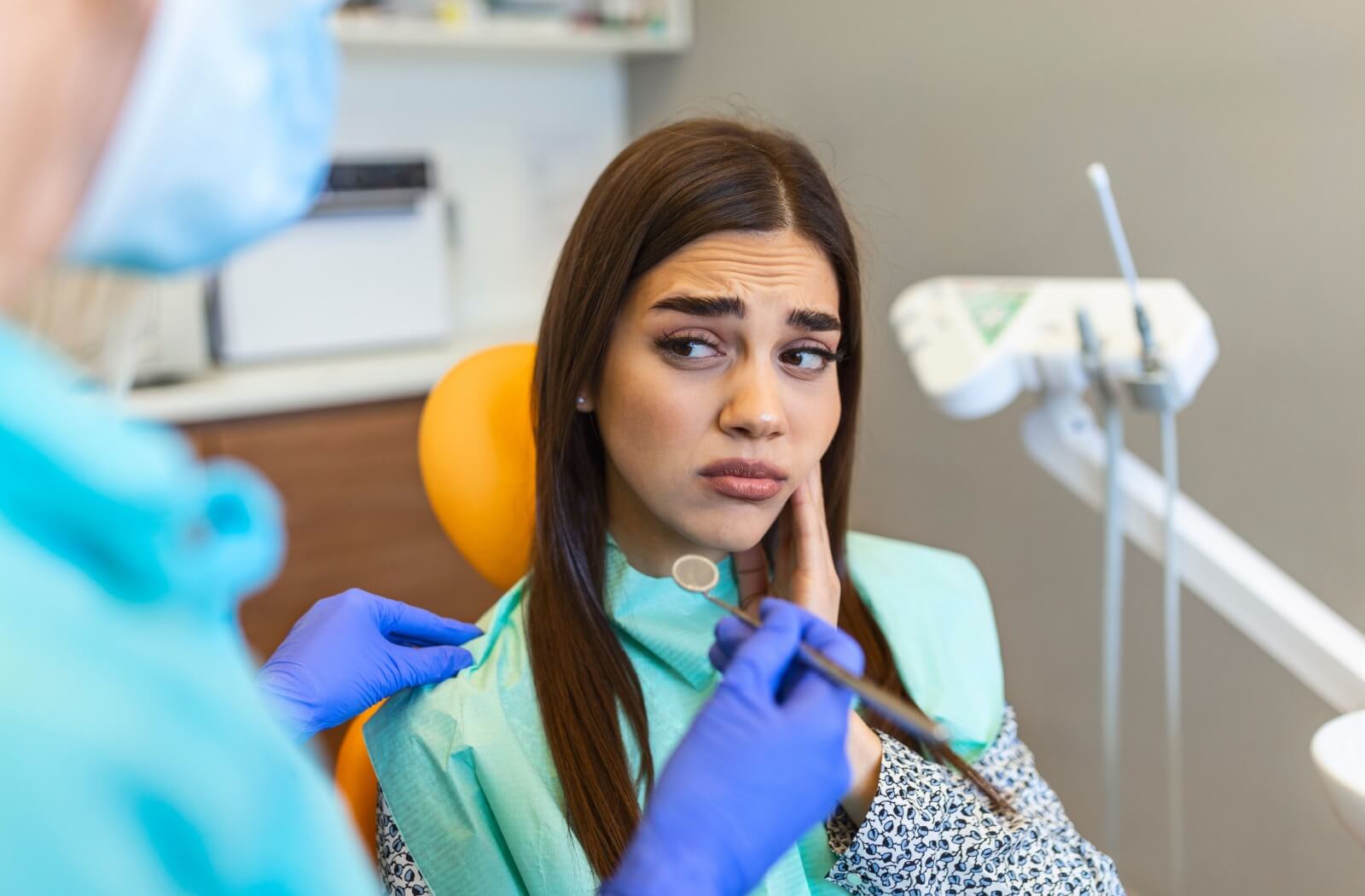 An individual sitting in a dental chair looking concerned while holding their jaw during an exam.